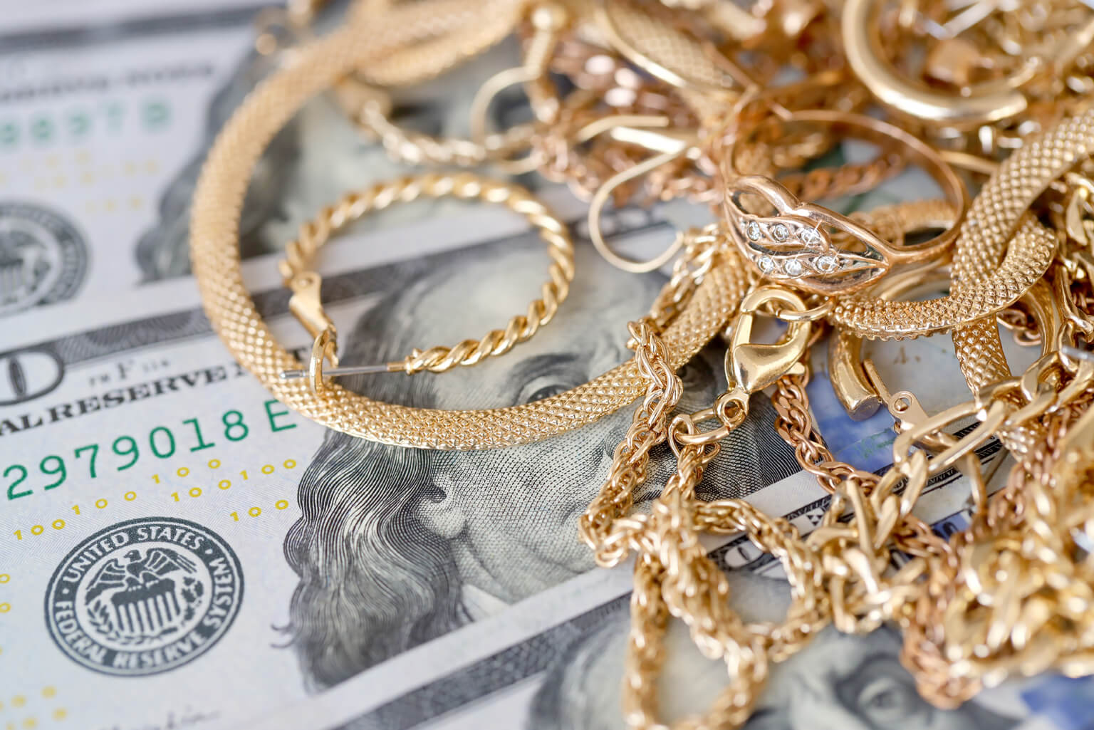 a pile of gold chains sitting on top of a hundred dollar bill